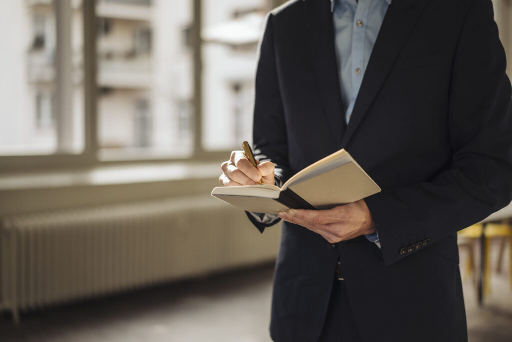 A business professional taking notes while standing in an office hallway.