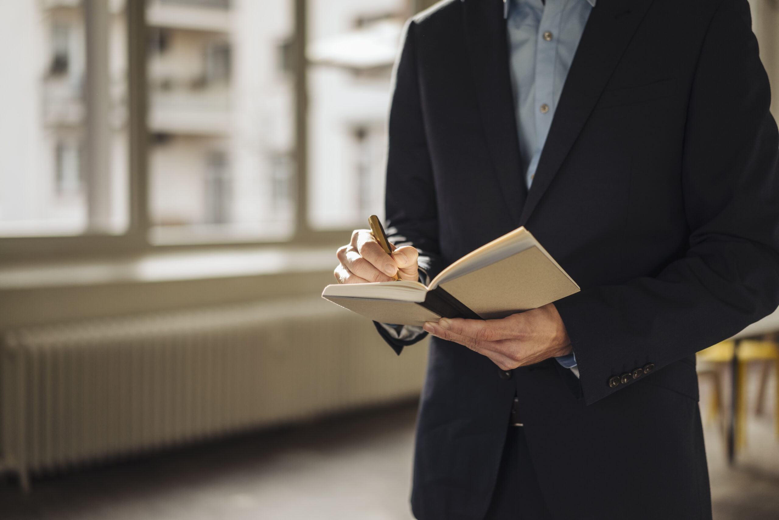 A business professional taking notes while standing in an office hallway.