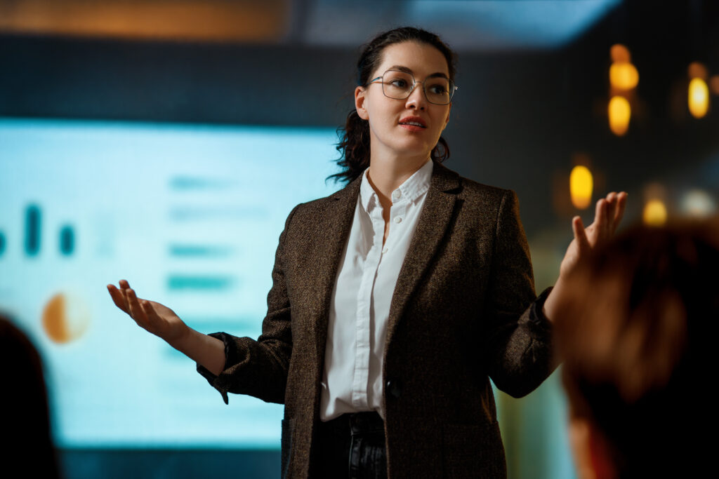 A young professional presenting in front of a screen showing charts and graphs